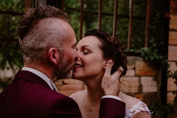Un couple heureux dans des costumes de mariage raffinés, partageant un moment tendre dans un décor verdoyant.