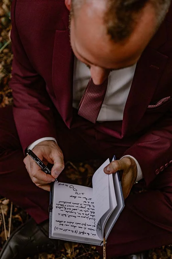Un marié en costume rouge intime et inspiré écrit dans un journal, créant un moment romantique et personnel.