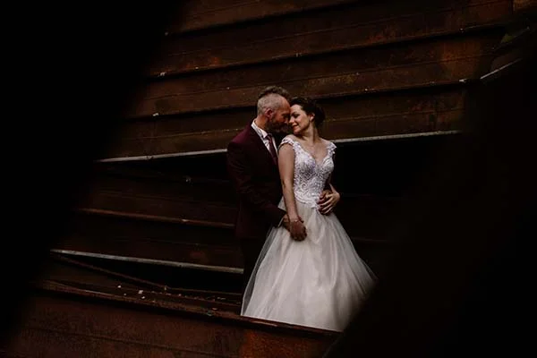 Un couple romantique sur les escaliers, la mariée dans un magnifique robe blanche détaillée et le mari dans un costume