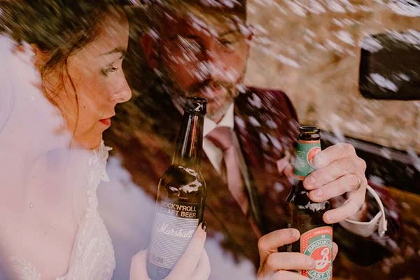Une jeune mariée et son mari partagent un moment détendu avec des bières de marque, incarnant l'ambiance décontractée