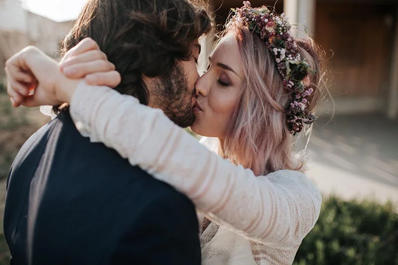 Jeune couple s'embrassant avec tendresse, la mariée portant une couronne de fleurs séchées dans un style bohème.