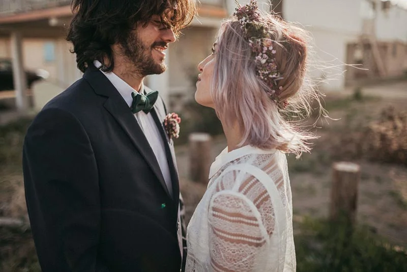 Couple en tenue de mariage folk se regardant avec tendresse, elle portant une couronne de fleurs et lui un nœud papillon.