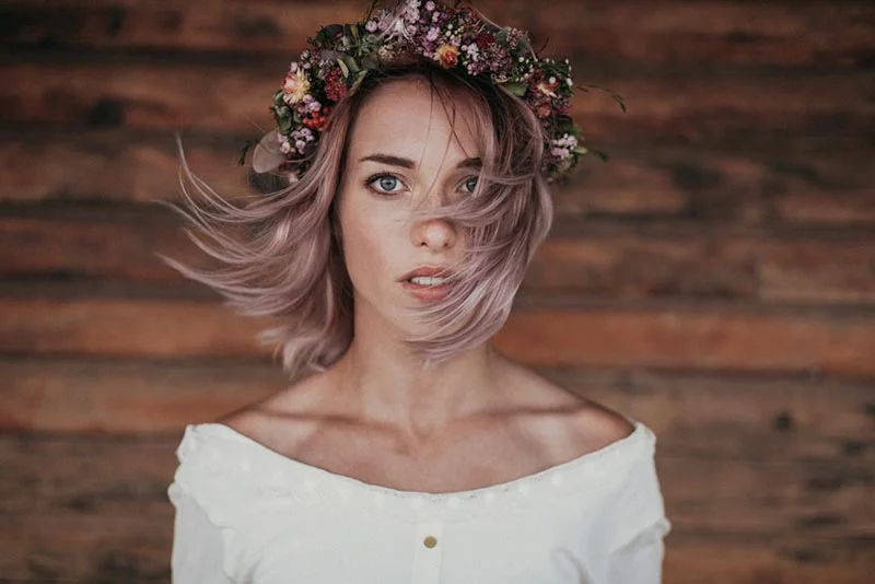 Jeune femme aux cheveux pastel portant une couronne de fleurs sauvages, style bohème et folk sur fond de bois.