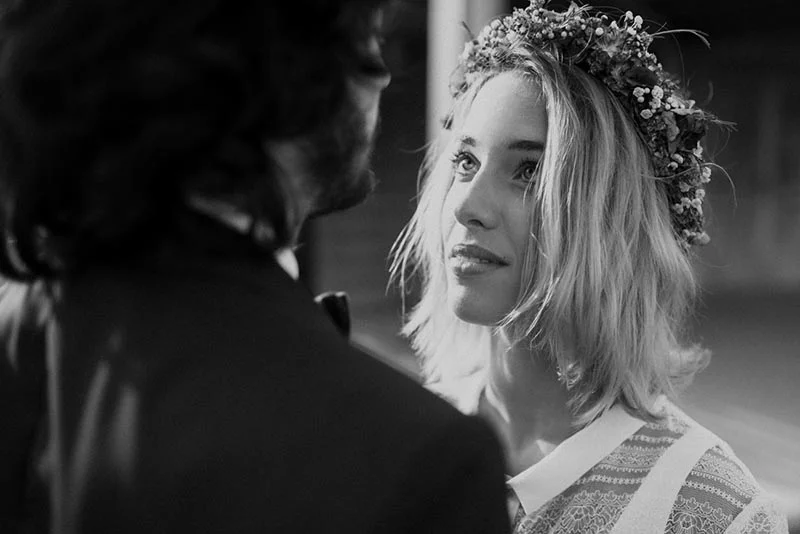 Portrait en noir et blanc d'un couple folk, la mariée portant une couronne de fleurs et regardant son époux.