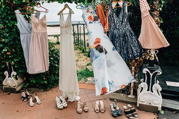 Plusieurs robes de cocktail et de soirée aux tons clairs et bleus suspendues en extérieur avec des chaussures assorties.
