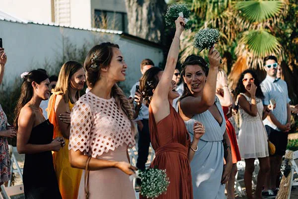 Des demoiselles d'honneur souriantes et élégantes lancent des bouquets lors d'un mariage chic et solaire à Barcelone.