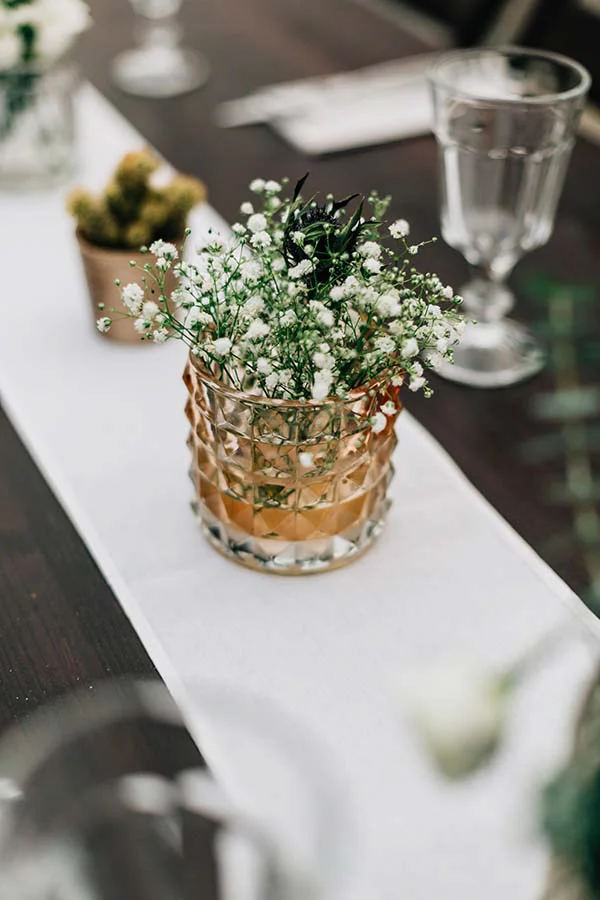 Centre de table bohème avec gypsophile dans un vase doré sur un chemin de table blanc, ambiance chic et lumineuse.