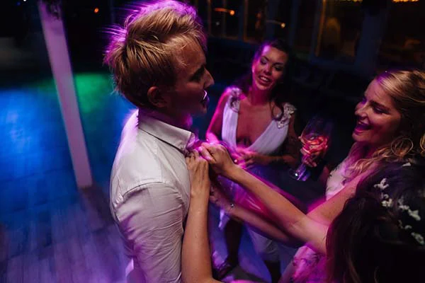 Un jeune homme et deux femmes rient et s'amusent lors d'une soirée festive aux lumières colorées.