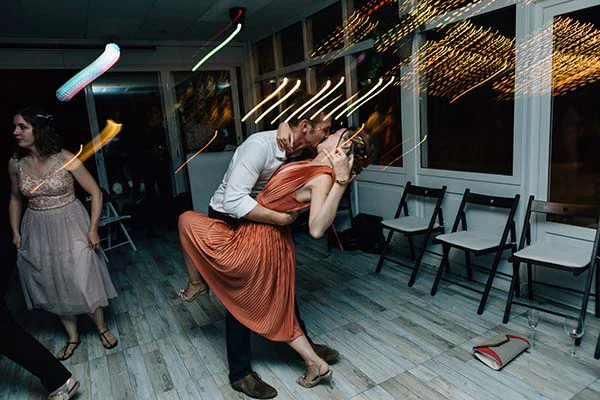 Un couple s'embrasse avec passion lors d'une danse festive, entouré de traînées lumineuses et d'une ambiance dynamique.