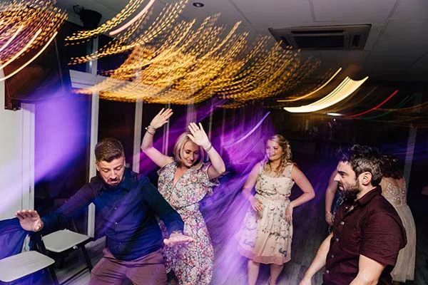 Invités dansant avec enthousiasme sous des jeux de lumières colorées et dynamiques lors d'une soirée de mariage.