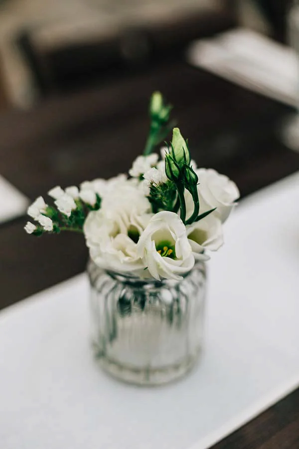 Petit bouquet de fleurs blanches dans un vase en verre strié sur un chemin de table blanc, ambiance chic et épurée.