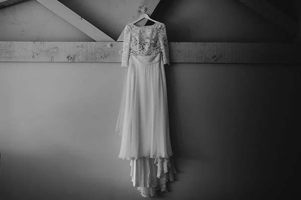 Robe de mariée blanche en dentelle et mousseline suspendue dans un intérieur épuré, photographie en noir et blanc.