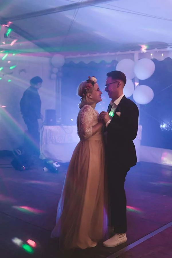 Jeunes mariés dansant sous des lumières colorées et bleutées lors d'une soirée festive et romantique.