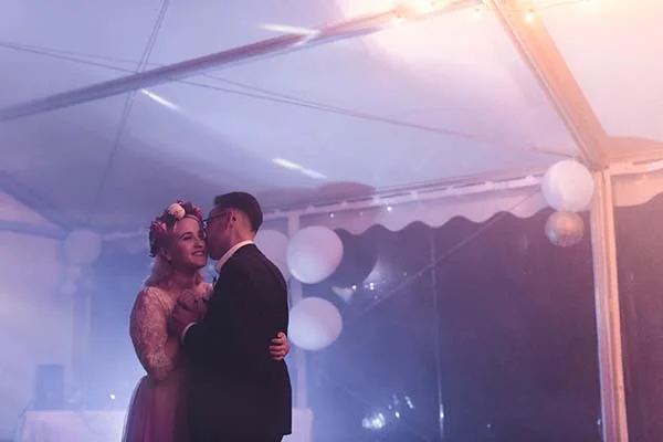 Jeunes mariés s'enlaçant sous un chapiteau illuminé dans une ambiance romantique aux tons pastel et vaporeux.
