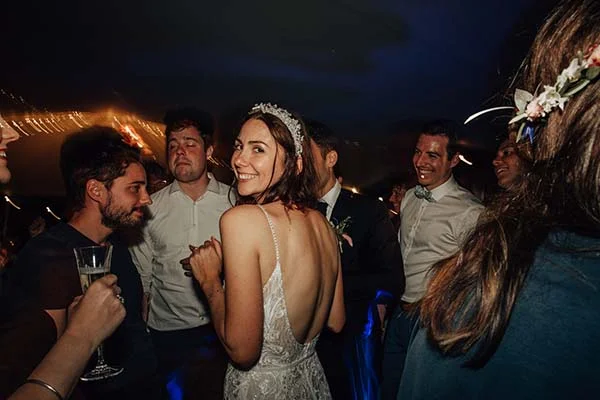 Une mariée rayonnante en robe blanche et diadème danse avec ses invités lors d'une soirée festive et chaleureuse.
