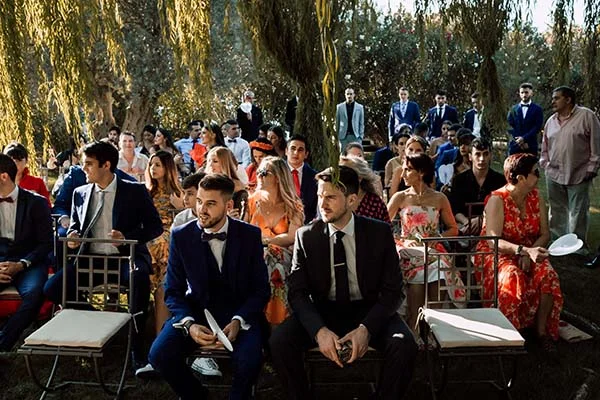 Invités élégants assis en plein air sous des saules pleureurs lors d'une cérémonie de mariage ensoleillée à Madrid.