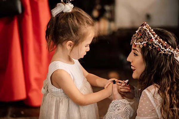 Une petite fille en robe blanche regarde tendrement la mariée coiffée d'une couronne bohème.