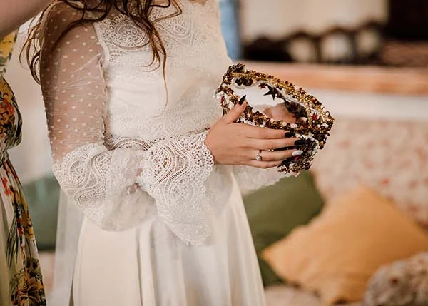 Mariée en robe blanche bohème à dentelle tenant un diadème doré et coloré.