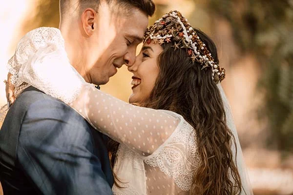 Couple enlacé dans une ambiance bohème, la mariée portant une couronne d'étoiles de mer et une robe en dentelle blanche.