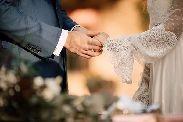 Gros plan sur les mains entrelacées d'un couple en tenue de mariage, ambiance romantique et lumineuse.