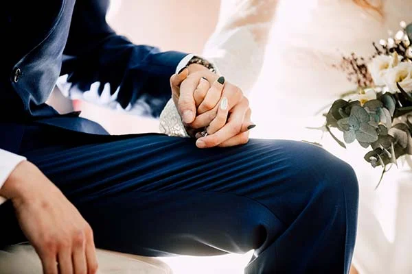 Gros plan sur les mains entrelacées d'un couple en tenue de mariage, dans une ambiance lumineuse et romantique.
