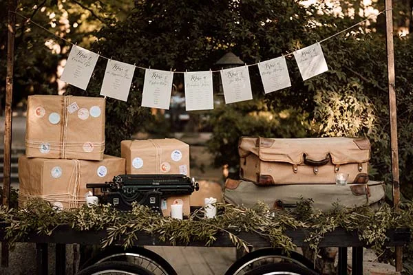 Décoration de mariage bohème avec machine à écrire, valises vintage et guirlande de cartes sur un chariot en bois.