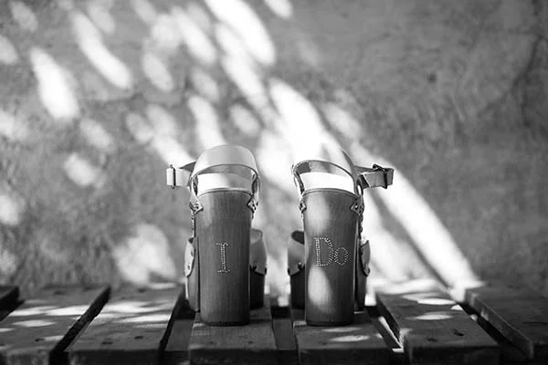 Chaussures compensées personnalisées en noir et blanc, posées sur un support en bois sous une lumière tamisée.