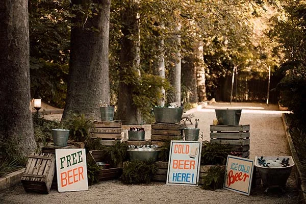 Buffet de bières fraîches dans des seaux en métal et caisses en bois, sous des arbres, pour un mariage bohème.