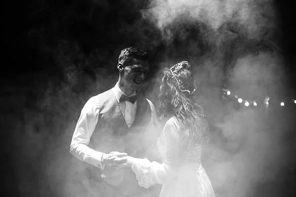 Couple de mariés souriants dansant dans un nuage de fumée, photographie artistique en noir et blanc.