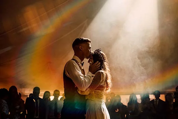 Silhouette d'un couple s'embrassant sous un faisceau de lumière et un arc-en-ciel vaporeux lors d'une fête festive.