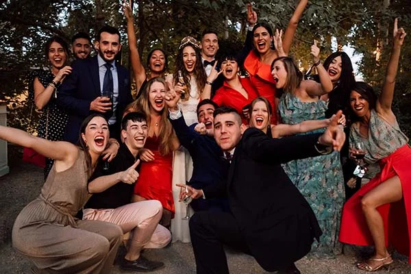 Groupe d'invités joyeux et colorés posant de manière décontractée lors d'un mariage festif en extérieur.