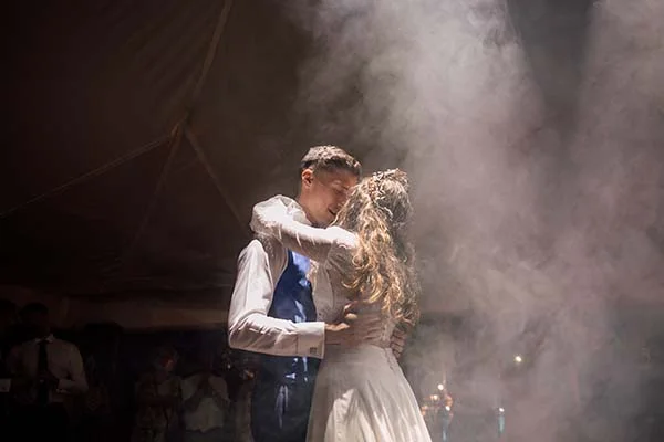 Jeunes mariés s'enlaçant lors d'une danse romantique entourés de fumée blanche dans une ambiance festive et vaporeuse.