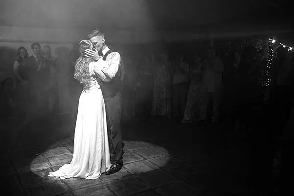 Couple de mariés s'embrassant dans une ambiance brumeuse et contrastée, photo en noir et blanc.