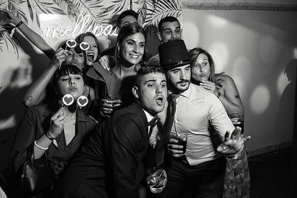 Groupe d'invités souriants et festifs posant dans un photobooth en noir et blanc avec des accessoires amusants.