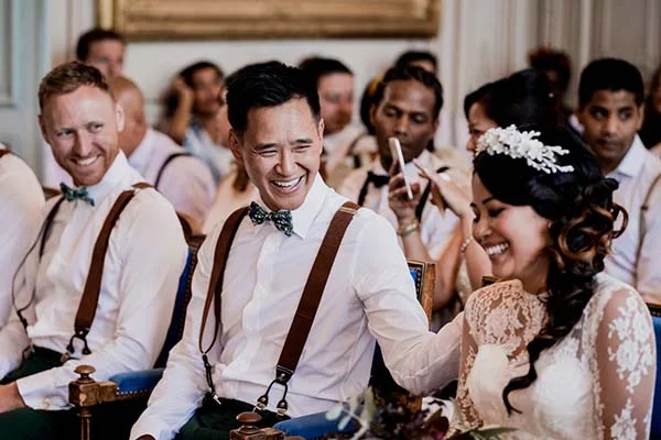 Jeunes mariés et invités souriants en tenue bohème blanche et bretelles lors d'une cérémonie chaleureuse.