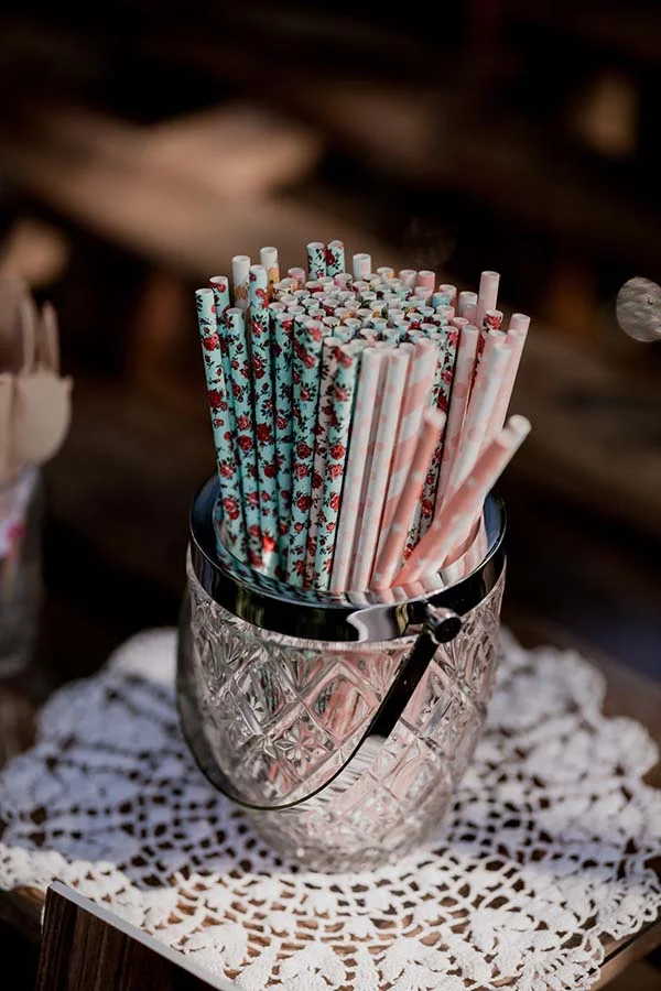 Pailles en papier colorées et à motifs dans un seau argenté posé sur un napperon en dentelle blanche.