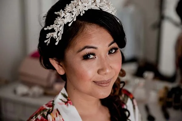 Portrait d'une mariée souriante avec un accessoire floral blanc dans les cheveux et un peignoir à motifs colorés.