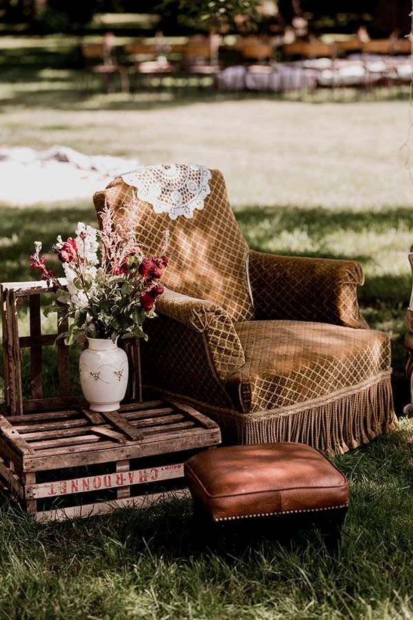 Fauteuil vintage en velours moutarde et caisses en bois avec fleurs blanches dans un jardin, ambiance bohème.