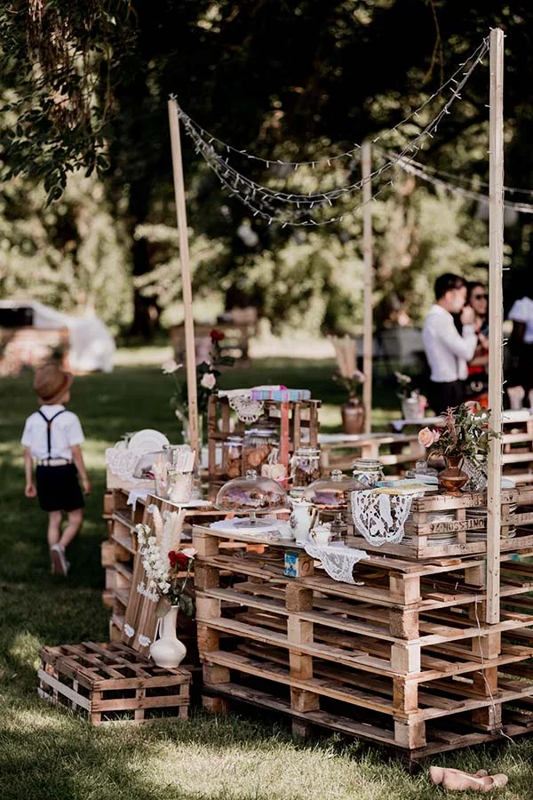 Buffet de mariage bohème installé sur des palettes en bois avec décorations artisanales et guirlandes lumineuses.