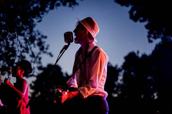 Musicien au chapeau chantant au micro lors d'une soirée de mariage bohème sous un ciel crépusculaire.