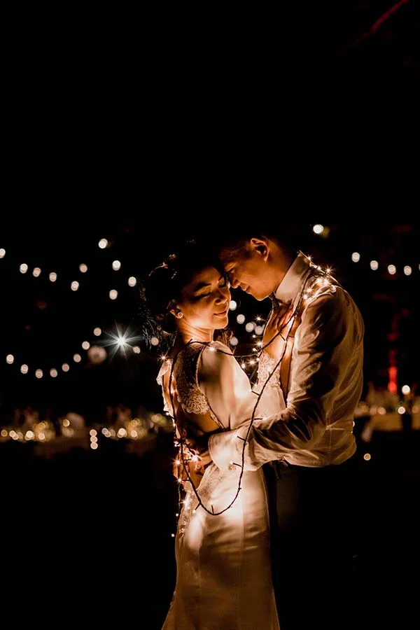 Couple d'amoureux enlacés dans l'obscurité, illuminés par une guirlande lumineuse chaleureuse.