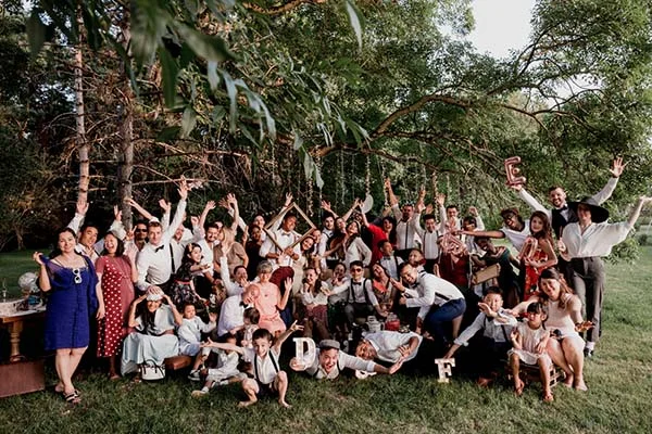 Groupe d'invités souriants et décontractés posant ensemble dans un jardin verdoyant lors d'un mariage bohème.