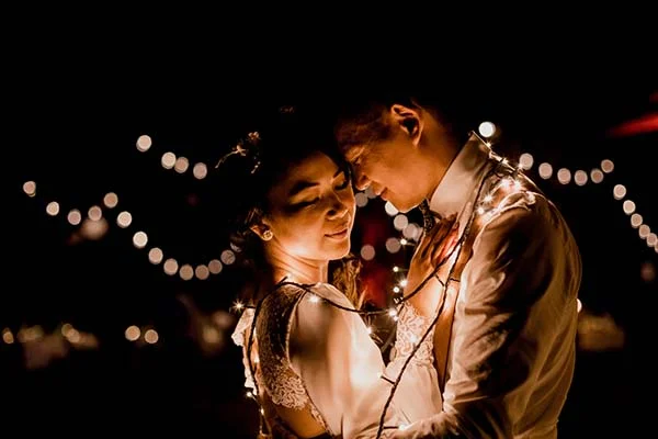 Couple d'amoureux enlacés dans l'obscurité, entourés de guirlandes lumineuses chaleureuses pour une ambiance romantique.