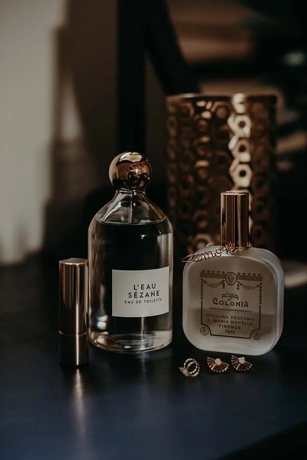 Flacons de parfums et bijoux dorés posés sur une surface sombre dans une ambiance élégante et feutrée.