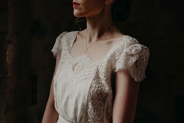 Profil d'une mariée en robe de dentelle blanche et rouge à lèvres vif dans une ambiance tamisée et romantique.