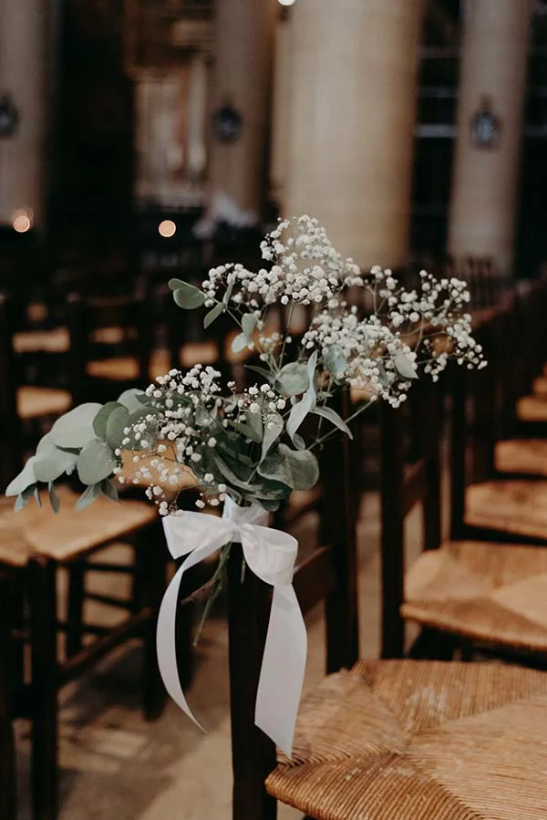 Composition florale de gypsophile et d'eucalyptus nouée d'un ruban blanc sur une chaise en bois sombre.
