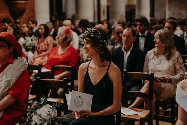 Invitée élégante en robe noire et couronne de fleurs parmi les convives lors du mariage d'Armony et Alexis.