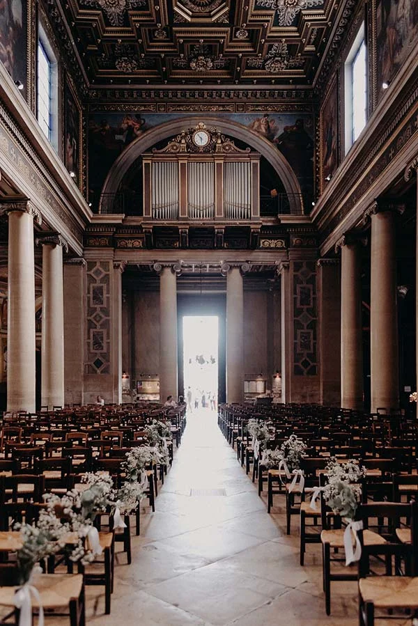Intérieur d'une église majestueuse avec allée centrale fleurie et rangées de chaises en bois pour une cérémonie.