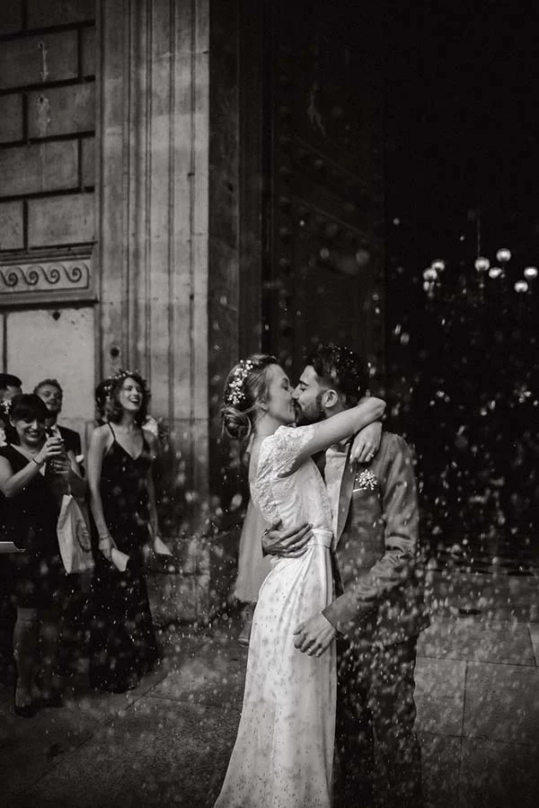 Jeunes mariés s'embrassant sous une pluie de confettis, photo en noir et blanc à l'ambiance romantique et festive.