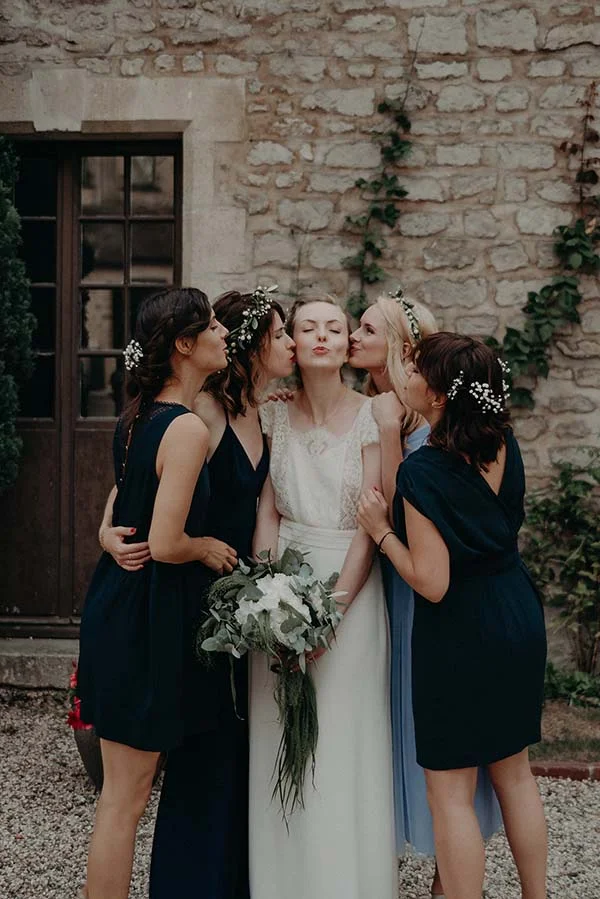 Une mariée en robe blanche entourée de ses demoiselles d'honneur en robes bleu marine et bleu clair pour un baiser groupé.